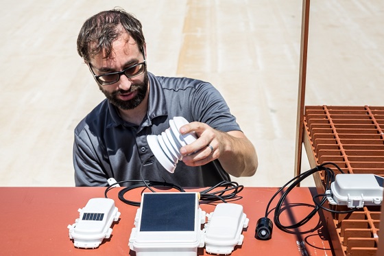 Peter Hamstra, an engineering manager with Resource Innovations, connects weather, radiation, and cellular transmitters before attaching them to a tower. The temperature and humidity probes measure the effectiveness of EnKoat's IntelliKoat roof coating. Photo courtesy of Charlie Leight, ASU News.